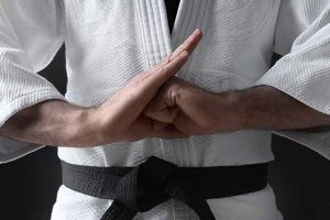 black belt martial arts student dressed in gi posing with their knuckle inside their opposing hands palm