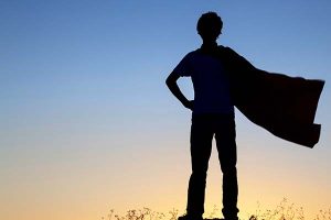 a silhouette of a young boy with a cape on, in the background there is a sunset. the boy looks like a superhero that wears a cape
