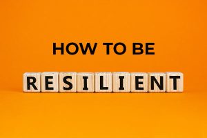 the words "how to be resilient" in front of an orange background. the word "resilient" is spelled with scrabble letter pieces