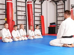 a black belt martial arts instructor dressed in gi sitting on the dojo floor addressing multiple students also dressed in gi