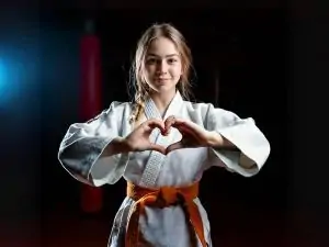 an orange belt martial arts student expressing kindness and empathy by forming a heart with their hands