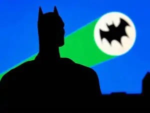 the bat signal shining bright in the night and a shadowing figure of a man staring at it triumphantly